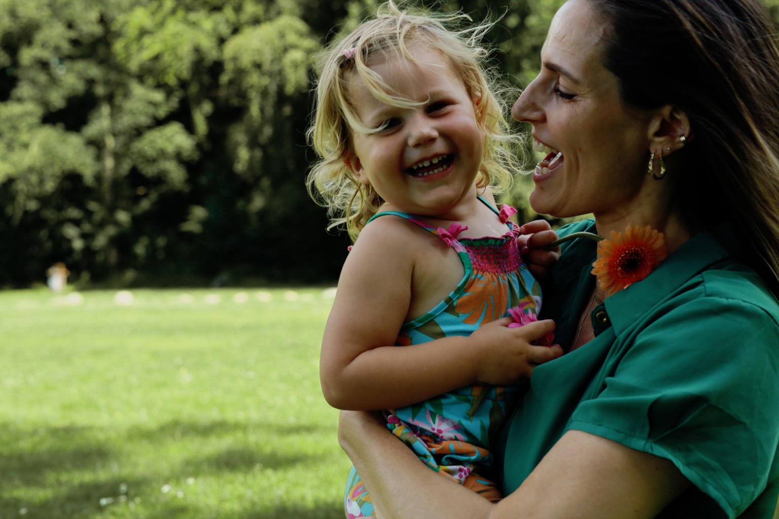 Ilona houdt een lachend kind vast in een zonnig veld