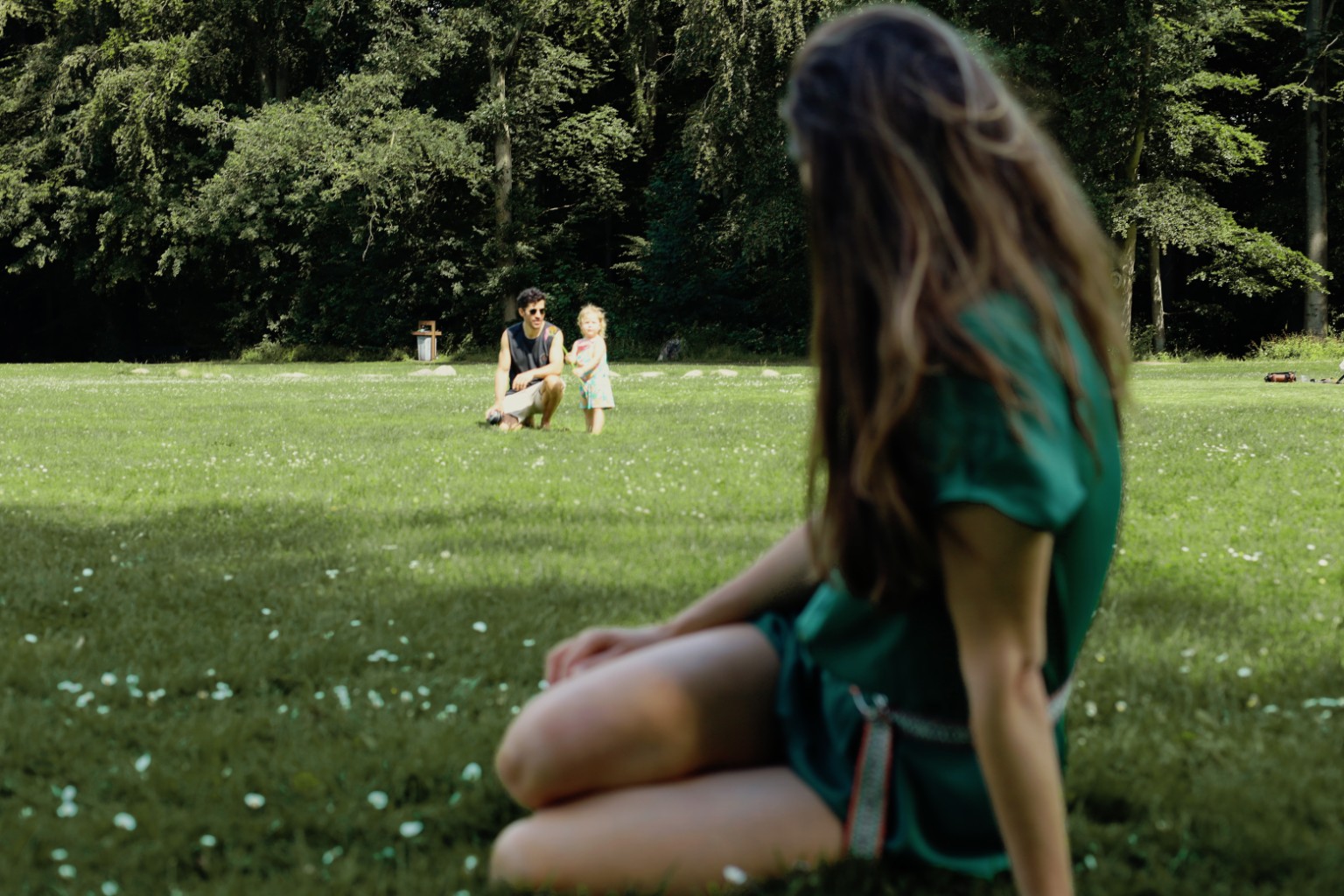 Ilona zit in het gras en kijkt naar een volwassene en een kind verderop in het veld
